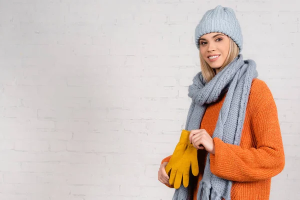 Femme gaie en tricot portant des gants près du mur de briques blanches — Photo de stock