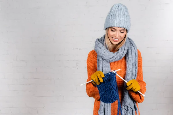 Jeune femme positive dans des gants chauds un pull tricotant avec du fil de laine sur fond blanc — Photo de stock