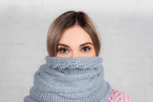 Jeune femme enveloppée dans une écharpe tricotée regardant la caméra sur fond gris — Photo de stock