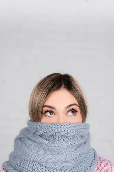 Femme enveloppée dans une écharpe tricotée regardant vers le haut sur fond blanc — Photo de stock