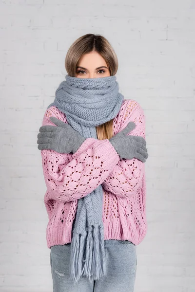 Mujer joven en prendas de punto y guantes que sufren de frío sobre fondo blanco - foto de stock