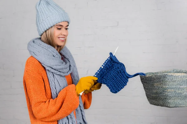 Mulher sorridente em malhas tricô perto da cesta no fundo branco — Fotografia de Stock