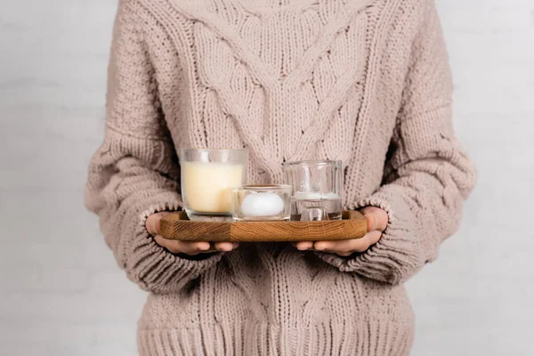 Vista ritagliata della donna in maglione caldo con candele su tavola di legno su sfondo bianco — Foto stock