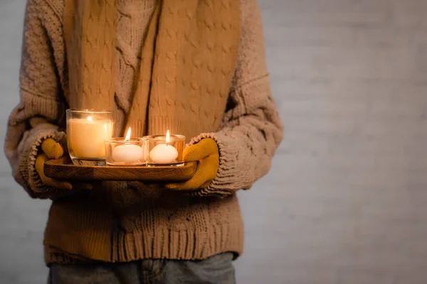 Cropped view of burning candles in hands of woman in warm clothes and gloves on grey background — Stock Photo