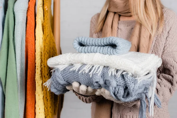 Vista ritagliata di donna che tiene maglieria vicino appendiabiti rack con maglioni su sfondo bianco — Foto stock