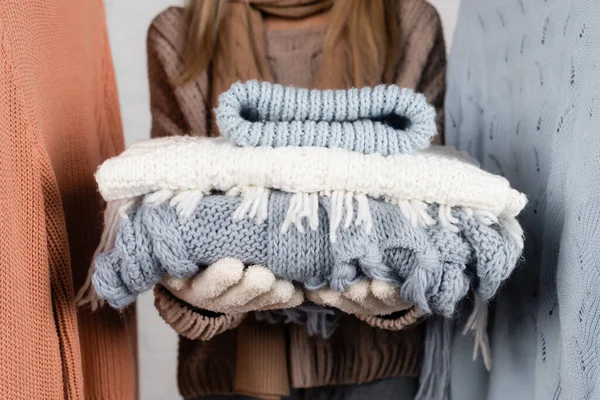 Cropped view of knitwear in hands of woman on blurred background near sweaters on white background — Stock Photo