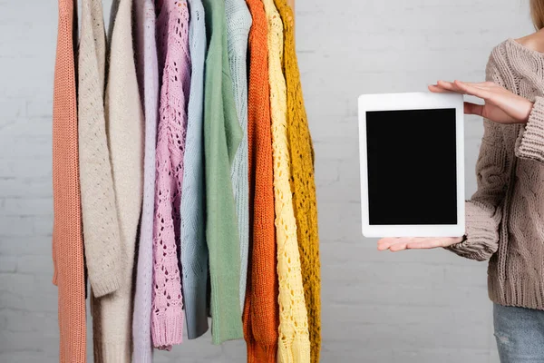 Vista recortada de la mujer sosteniendo tableta digital con pantalla en blanco cerca de suéteres calientes sobre fondo blanco - foto de stock