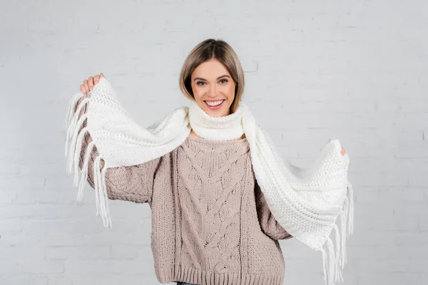 Femme souriante en pull tricoté tenant écharpe sur fond blanc — Photo de stock