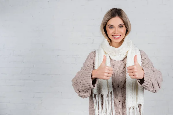 Young smiling woman in sweater and scarf showing thumbs up on white background — Stock Photo