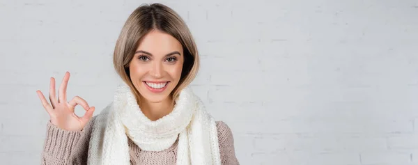 Jovem mulher em cachecol de malha e suéter mostrando gesto ok no fundo branco, banner — Fotografia de Stock