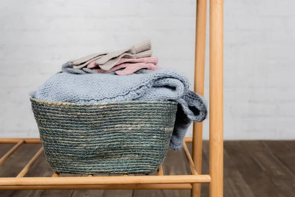 Gloves and warm knitted sweater in basket on hanger rack — Stock Photo