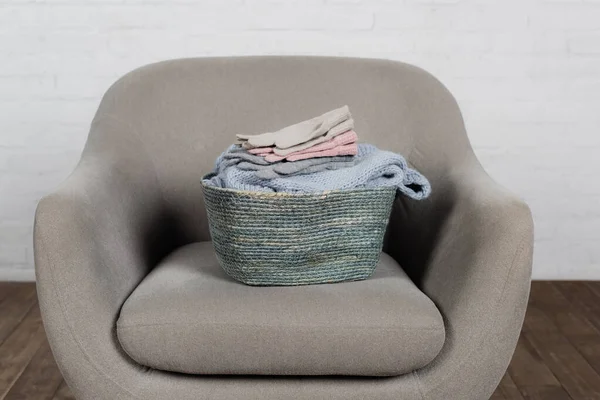 Cesta con suéter de punto y guantes en sillón en casa - foto de stock