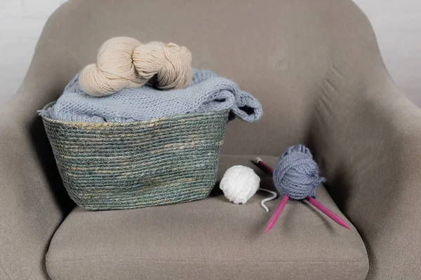 Basket with woolen yarn and knitting needles on armchair on white background — Stock Photo