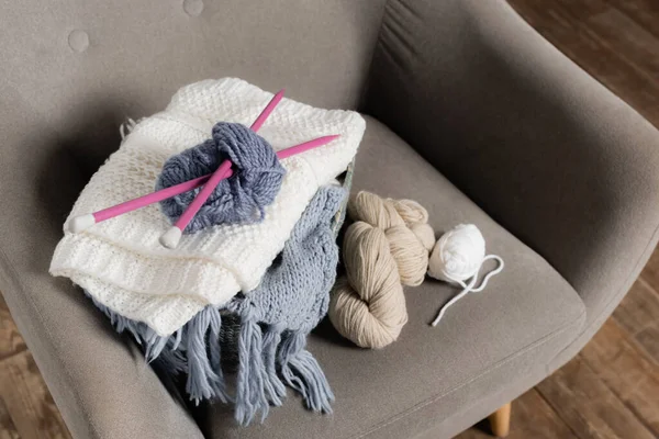 Vista de ángulo alto de tejer innecesario, hilo y suéter en el sillón en casa - foto de stock