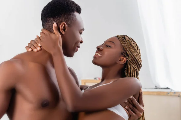Smiling african american woman in bra embracing neck of shirtless boyfriend at home — Stock Photo