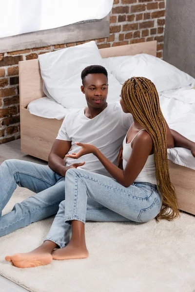 Mujer afroamericana hablando con novio cerca de la cama en el suelo - foto de stock