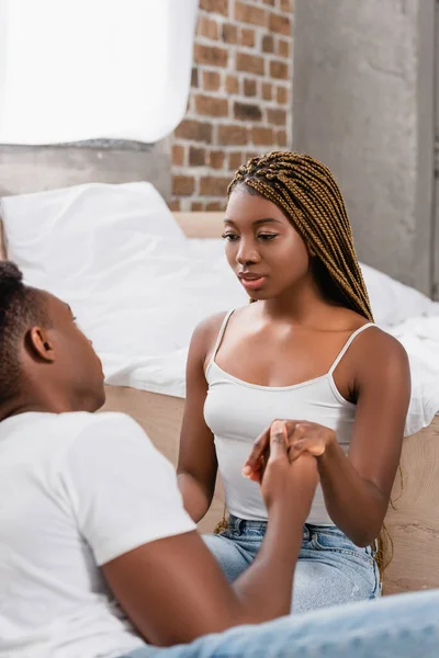 Mujer afroamericana cogida de la mano con su novio en primer plano borroso en el dormitorio - foto de stock
