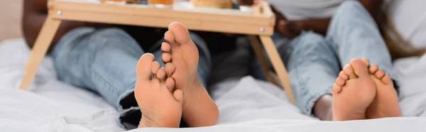 Vista cortada de pés de casal afro-americano na cama no fundo borrado, banner — Fotografia de Stock