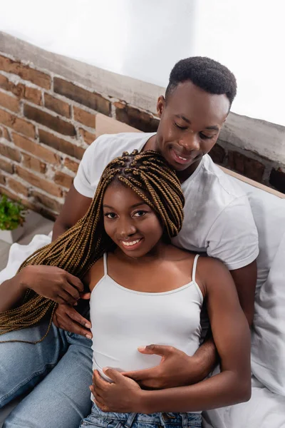 Vista de alto ângulo do homem afro-americano abraçando a namorada sorridente na cama — Fotografia de Stock