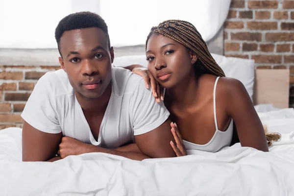 African american couple looking at camera on bed — Stock Photo