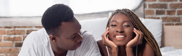 Alegre mujer afroamericana mirando la cámara cerca de novio en casa, pancarta - foto de stock