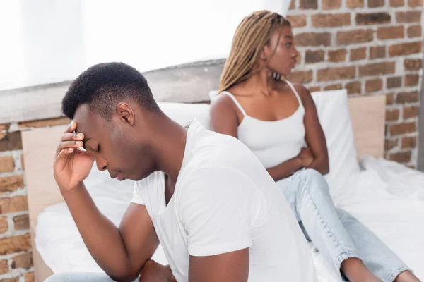 Homme afro-américain bouleversé assis près de la petite amie sur le lit sur fond flou — Photo de stock