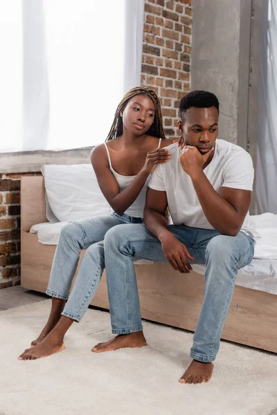African american woman calming pensive boyfriend on bed — Stock Photo