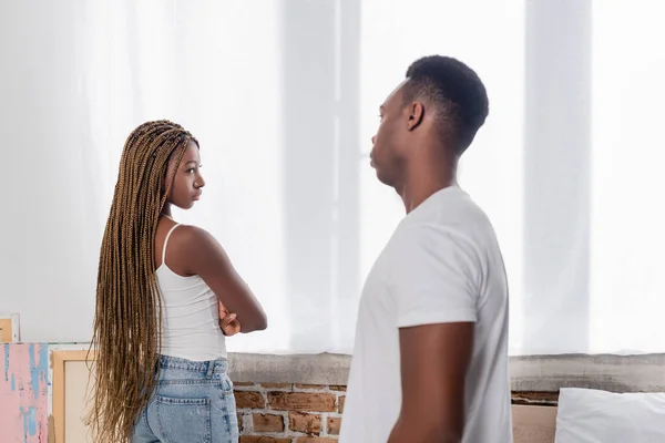 Offended african american woman looking at boyfriend on blurred foreground at home — Stock Photo