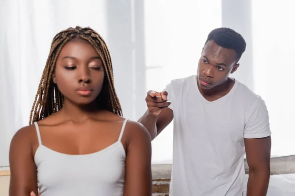 African american man pointing with finger at girlfriend on blurred foreground while quarrelling at home — Stock Photo