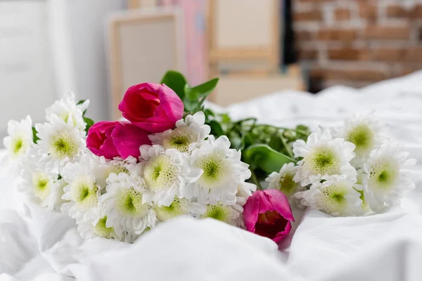 Crisantemos y tulipanes sobre ropa de cama blanca en primer plano borroso - foto de stock