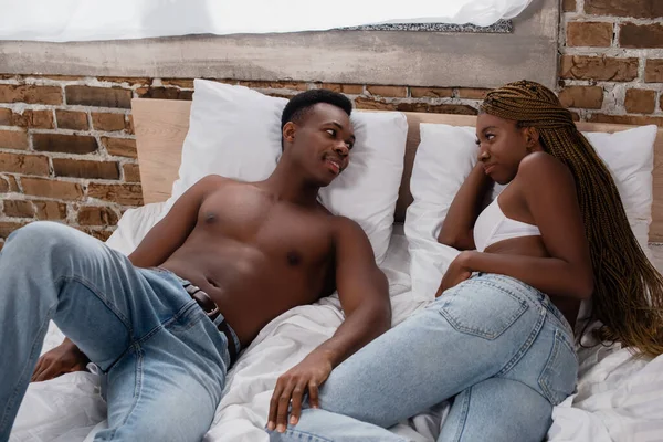 Smiling african american man looking at sexy woman on bed — Stock Photo