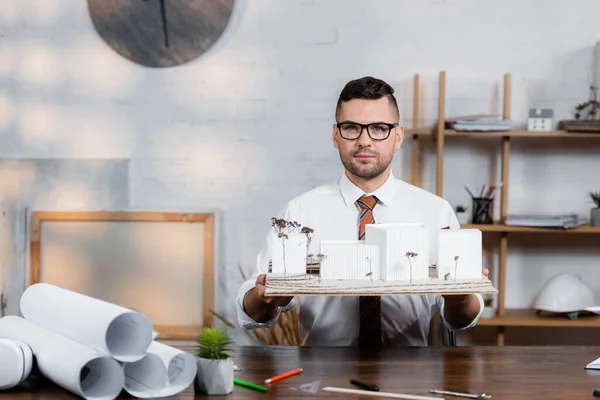 Selbstbewusster Architekt, der in die Kamera blickt, während er architektonische Maquette hält — Stockfoto