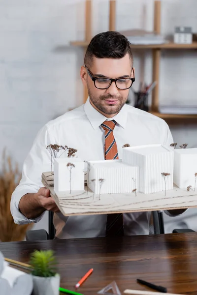 Positiver Architekt, der architektonische Maquette im Amt hält, verschwommener Vordergrund — Stockfoto