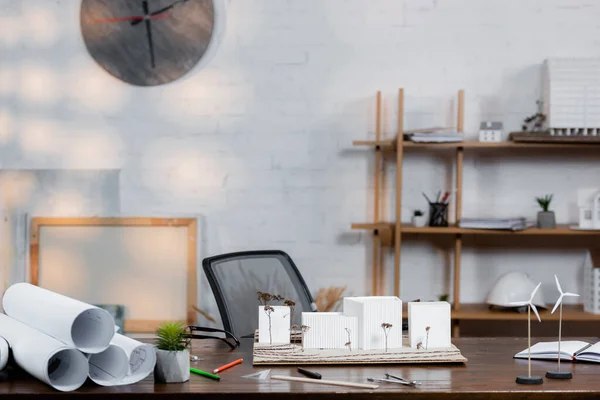 Rolled blueprints, architectural maquette, and wind turbines models on desk in office — Stock Photo