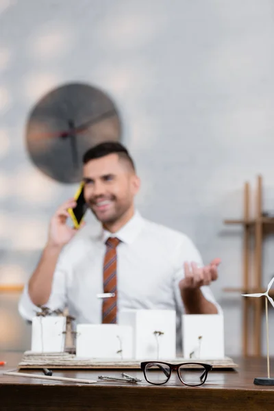 Felice architetto parlando sul telefono cellulare vicino progetto architettonico, sfondo sfocato — Foto stock