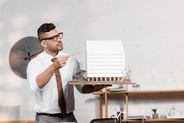 Architecte sérieux dans les lunettes pointant avec crayon à la maison modèle — Photo de stock