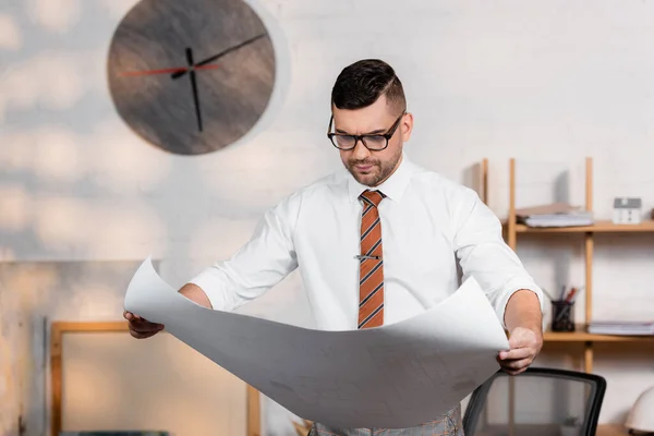 Thoughtful architect in eyeglasses holding blueprint in office — Stock Photo