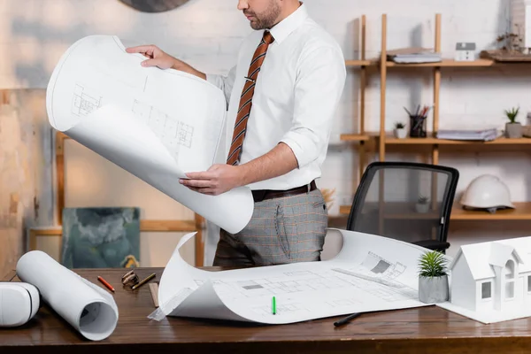 Cropped view of architect holding blueprint near plans and house model on desk — Stock Photo