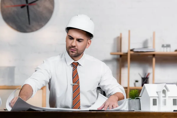 Architecte concentré dans le casque travaillant sur le projet près de maison modèle — Photo de stock