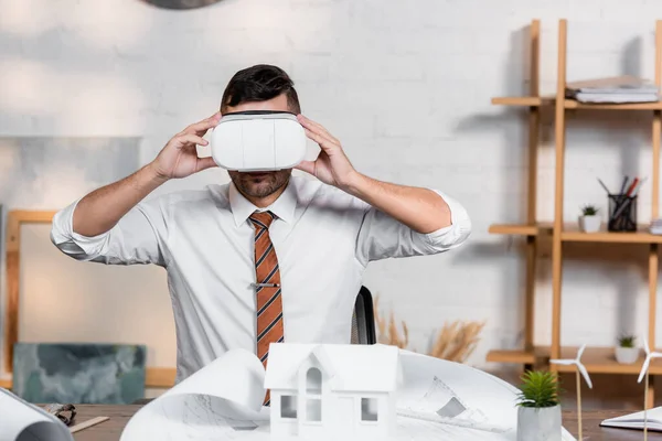 Architetto toccando auricolare vr sul posto di lavoro vicino progetto e modello di casa — Foto stock