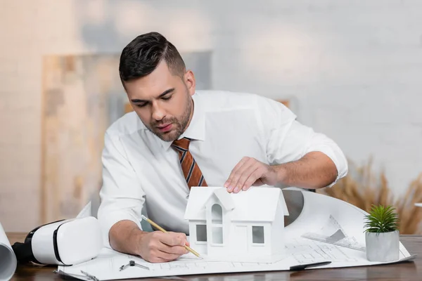 Concentré architecte dessin sur plan près de maison modèle — Photo de stock