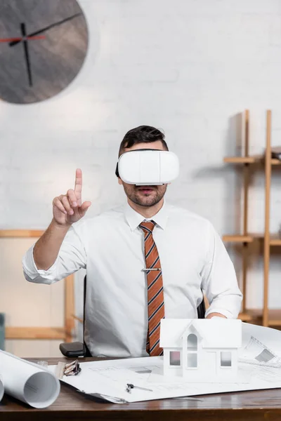 Arquitecto señalando con el dedo cerca de planos y modelo de casa en el escritorio - foto de stock