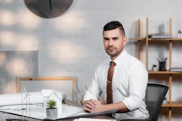 Serious architect looking at camera while sitting at workplace in architectural agency — Stock Photo