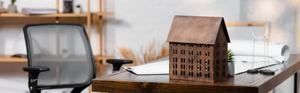 Modelo da casa perto de maquetes de turbinas eólicas na mesa em escritório de arquitetura, banner — Fotografia de Stock