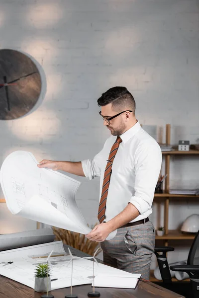 Arquiteto segurando planta perto de modelos de turbinas eólicas na mesa — Fotografia de Stock