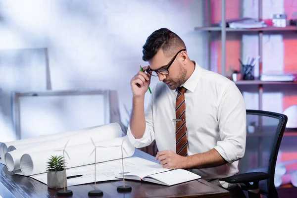 Arquitecto enfocado sosteniendo lápiz mientras trabajaba cerca de plano y cuaderno - foto de stock