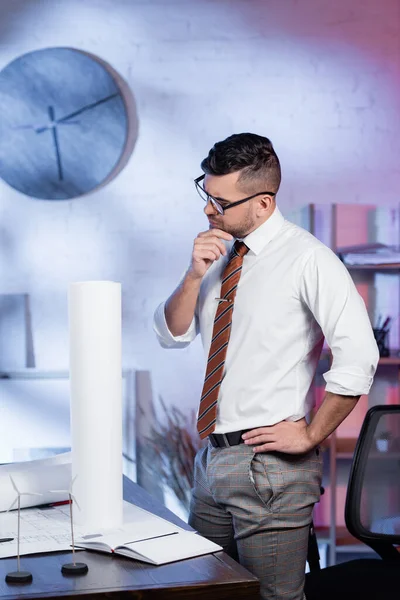 Вдумливий архітектор стоїть з рукою на стегні на робочому місці в офісі — стокове фото