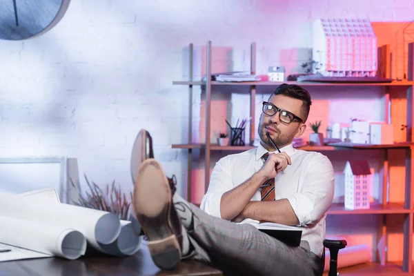 Architecte réfléchi regardant loin tout en étant assis avec les jambes sur le bureau — Photo de stock