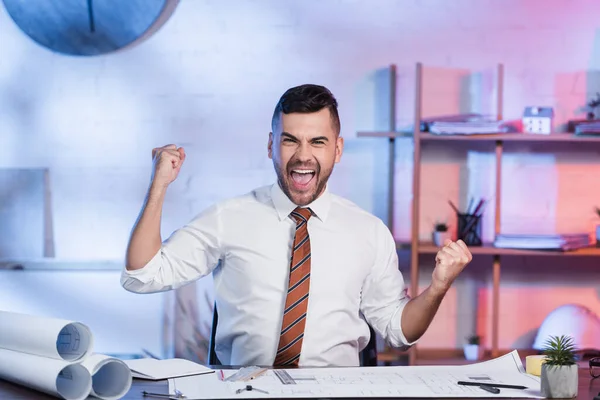 Excited architect showing success gesture near blueprints at workplace — Stock Photo