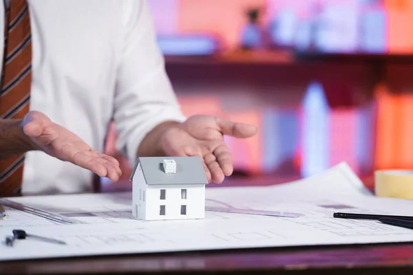 Partial view of architect pointing with hands at house maquette, blurred background — Stock Photo